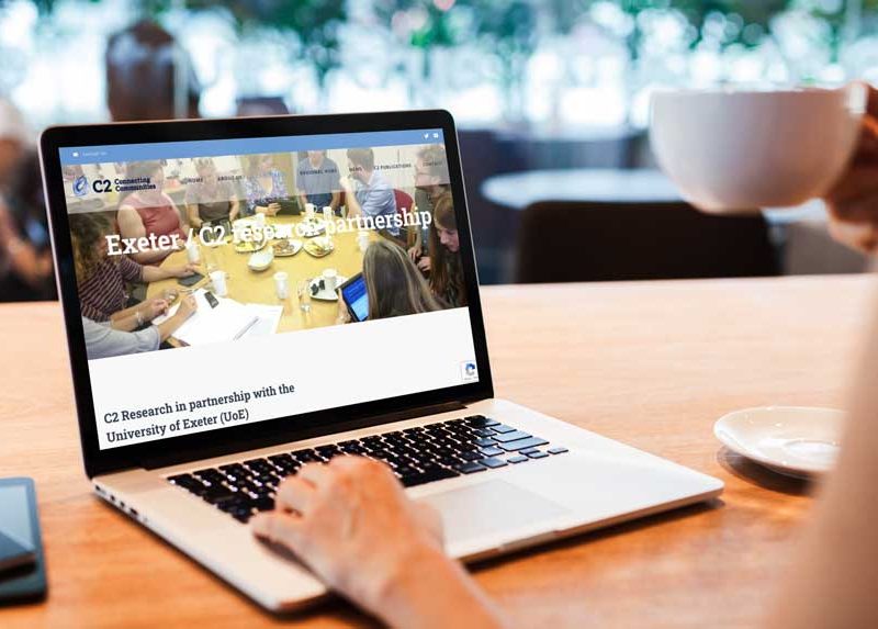 Woman looking at C2 website on macbook pro with a cup of coffee.